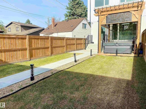 Expansive backyard featuring a manicured lawn, a concrete pathway bordered by decorative gravel, and perimeter wood fencing - 10936 117 Street, Edmonton, AB - Outdoor