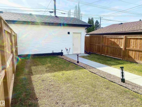 Detached garage with white siding and dark trim, featuring a concrete pathway flanked by gravel - 10936 117 Street, Edmonton, AB - Outdoor