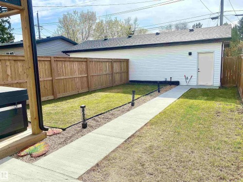 Expansive backyard featuring a new privacy fence, a concrete walkway, and a detached white-sided structure with a side entry door - 10936 117 Street, Edmonton, AB - Outdoor
