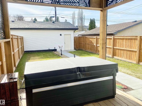 Expansive backyard featuring a hot tub on a wood deck, a concrete walkway, and a manicured lawn - 10936 117 Street, Edmonton, AB - Outdoor With Exterior