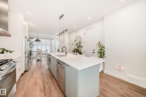 The kitchen features a large island with a sink and modern pendant lighting, stainless steel appliances, and light wood flooring - 10936 117 Street, Edmonton, AB - Indoor Photo Showing Kitchen With Upgraded Kitchen