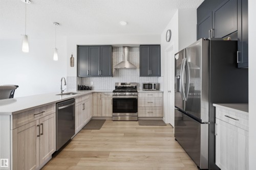 The kitchen features a blend of light wood and dark grey cabinetry, stainless steel appliances, and light wood flooring - 7017 54 Avenue, Beaumont, AB - Indoor Photo Showing Kitchen With Stainless Steel Kitchen With Upgraded Kitchen