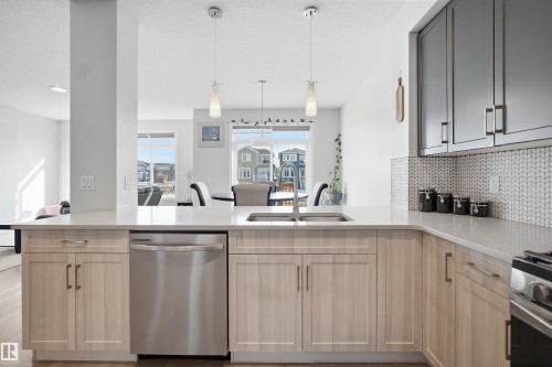 The kitchen features a double basin sink, stainless steel dishwasher, light wood cabinetry, and dark gray upper cabinets - 7017 54 Avenue, Beaumont, AB - Indoor Photo Showing Kitchen With Stainless Steel Kitchen With Double Sink With Upgraded Kitchen