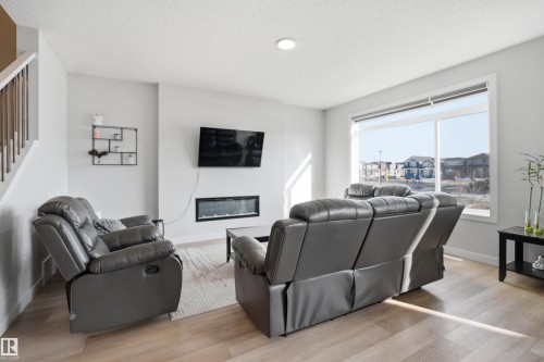 The living room features light-colored walls, a large window, and light wood-look flooring - 7017 54 Avenue, Beaumont, AB - Indoor Photo Showing Living Room With Fireplace