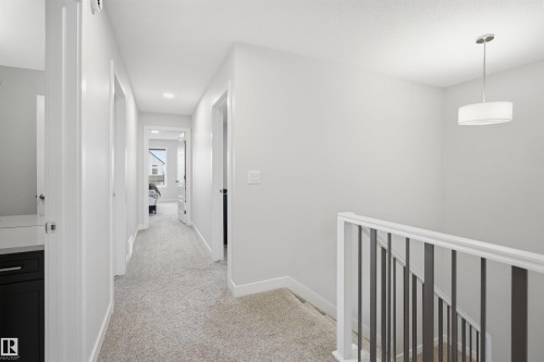 The property features a staircase with a white and dark railing, a hallway with light-colored carpeting, and a ceiling light fixture - 7017 54 Avenue, Beaumont, AB - Indoor Photo Showing Other Room