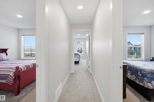 The property features a hallway with carpeted flooring, leading to several rooms, each with windows providing views of the surrounding neighborhood - 7017 54 Avenue, Beaumont, AB - Indoor Photo Showing Bedroom