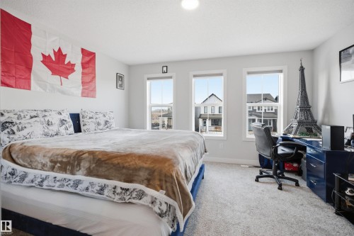 The room features three large windows that provide views of the surrounding neighborhood and a neutral color palette throughout - 7017 54 Avenue, Beaumont, AB - Indoor Photo Showing Bedroom