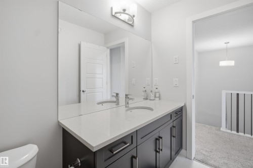 The bathroom features a dual sink vanity with a white countertop and dark cabinetry, complemented by a large wall-mounted mirror - 7017 54 Avenue, Beaumont, AB - Indoor Photo Showing Bathroom