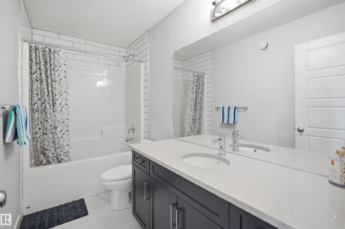 Modern bathroom featuring a double vanity with two sinks and a quartz countertop, a large mirror, a separate tub and shower combination with subway tile surround, and a sleek toilet - 7017 54 Avenue, Beaumont, AB - Indoor Photo Showing Bathroom