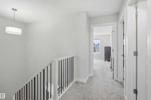 A neutral-toned hallway featuring light grey carpet, white walls, and a modern drum pendant light fixture - 7017 54 Avenue, Beaumont, AB - Indoor Photo Showing Other Room