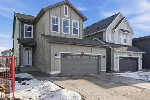 The property features a two-story exterior with light gray siding and white trim, a dark gray roof, and an integrated garage with a gray door - 7017 54 Avenue, Beaumont, AB - Outdoor With Facade