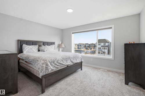 This room features a large window providing views of the surrounding neighborhood, light gray walls, and light gray carpet - 7017 54 Avenue, Beaumont, AB - Indoor Photo Showing Bedroom