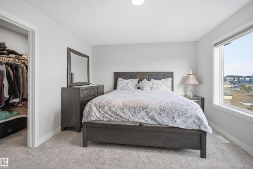 This bedroom features light gray carpeting, a large window, and a closet with a white frame - 7017 54 Avenue, Beaumont, AB - Indoor Photo Showing Bedroom