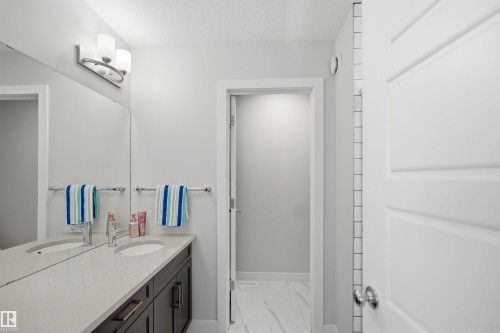 This bathroom features a double vanity with a light-colored countertop, two rectangular sinks with chrome faucets, and dark cabinetry - 7017 54 Avenue, Beaumont, AB - Indoor Photo Showing Bathroom