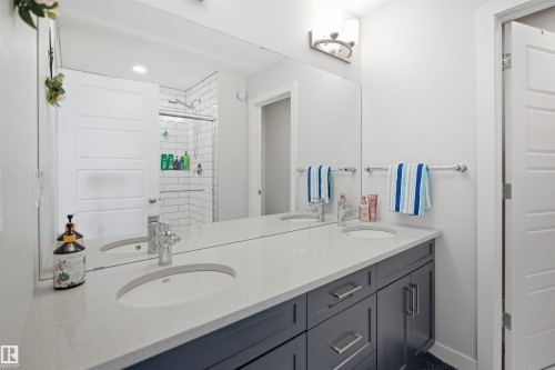 The bathroom features a dual vanity with a light-colored countertop, built-in sinks, and gray cabinetry with silver hardware - 7017 54 Avenue, Beaumont, AB - Indoor Photo Showing Bathroom