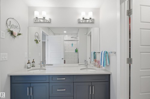 Bathroom featuring a dual vanity with a light-colored countertop and dark blue cabinetry, individual sinks, and a large mirror - 7017 54 Avenue, Beaumont, AB - Indoor Photo Showing Bathroom