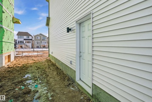 The property features white horizontal siding and a white entry door with a wall-mounted exterior light fixture - 7017 54 Avenue, Beaumont, AB - Outdoor