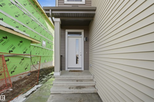 The property features a front entrance with concrete steps and a white door, set against siding - 7017 54 Avenue, Beaumont, AB - Outdoor