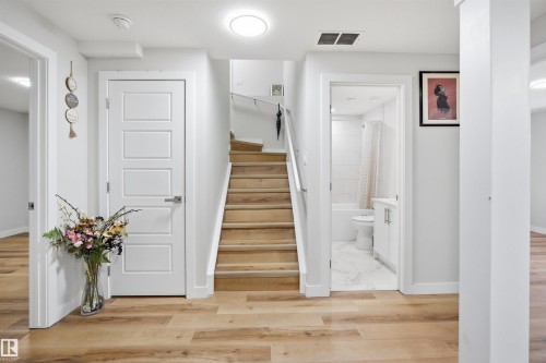 The property features light-toned hardwood flooring throughout the main areas, a wooden staircase, and a bathroom with a white vanity and tiled flooring - 7017 54 Avenue, Beaumont, AB - Indoor Photo Showing Other Room