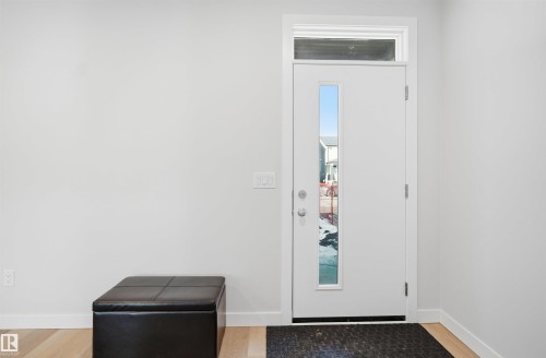 The entryway features a white front door with a vertical glass insert and a transom window, set against light-colored walls and light wood flooring - 7017 54 Avenue, Beaumont, AB - Indoor Photo Showing Other Room