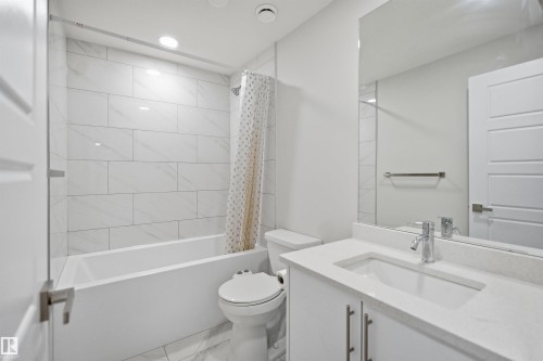 The bathroom features a vanity with a white countertop and a rectangular sink, a toilet, and a bathtub with white subway tile surround - 7017 54 Avenue, Beaumont, AB - Indoor Photo Showing Bathroom