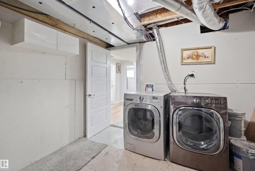 The property includes a laundry area with a front-loading washer and dryer, an overhead cabinet, and a white paneled door - 7017 54 Avenue, Beaumont, AB - Indoor Photo Showing Laundry Room