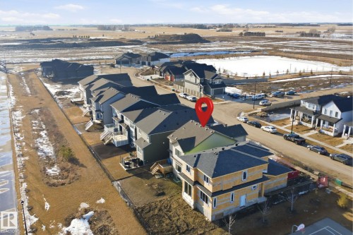 Aerial view of the property and a portion of the surrounding neighbourhood, featuring a paved road, other residential properties, and open fields in the distance - 7017 54 Avenue, Beaumont, AB - Outdoor With View