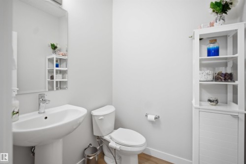 The bathroom features a pedestal sink with a chrome faucet, a toilet, and a large wall mirror - 7017 54 Avenue, Beaumont, AB - Indoor Photo Showing Bathroom