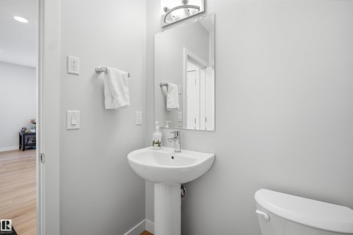 Bathroom featuring a pedestal sink, a wall-mounted mirror, and a toilet - 7017 54 Avenue, Beaumont, AB - Indoor Photo Showing Bathroom