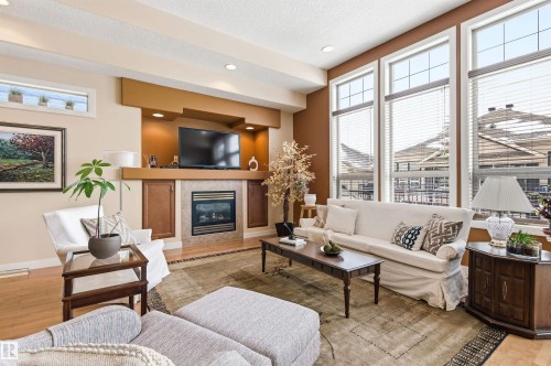 Living area featuring a fireplace with a stone surround, an integrated entertainment unit, and large windows with blinds - 13 841 156 Street, Edmonton, AB - Indoor Photo Showing Living Room With Fireplace