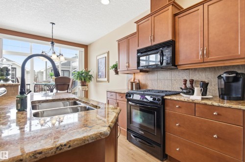 The kitchen features abundant wood cabinetry, granite countertops, a double basin sink, and a black range with an overhead microwave - 13 841 156 Street, Edmonton, AB - Indoor Photo Showing Kitchen With Double Sink