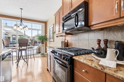 The kitchen features wood cabinetry, granite countertops, and a tile backsplash - 13 841 156 Street, Edmonton, AB - Indoor Photo Showing Kitchen