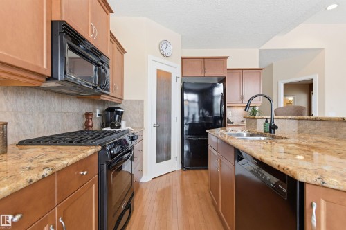 The kitchen features wood cabinetry, granite countertops, a black gas range, and a black refrigerator - 13 841 156 Street, Edmonton, AB - Indoor Photo Showing Kitchen With Double Sink