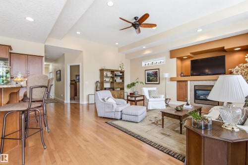 The open-concept living area features hardwood floors, a gas fireplace with a stone surround, and a ceiling fan - 13 841 156 Street, Edmonton, AB - Indoor Photo Showing Living Room With Fireplace
