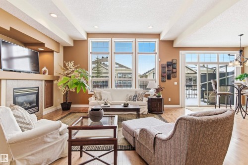 Living area featuring hardwood flooring, a gas fireplace with a tiled surround, and large windows providing ample natural light - 13 841 156 Street, Edmonton, AB - Indoor Photo Showing Living Room With Fireplace