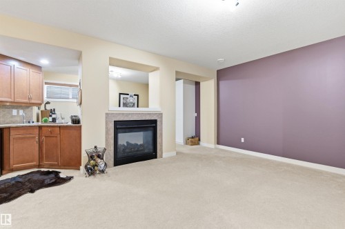 This living space features a fireplace with a stone surround, an integrated wet bar with wood cabinetry and a tiled backsplash, and carpeted flooring - 13 841 156 Street, Edmonton, AB - Indoor Photo Showing Other Room With Fireplace