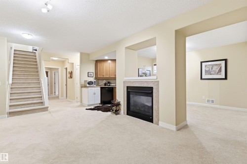 This inviting living area features plush carpeting, a staircase with a white railing, and a built-in fireplace with a stone surround - 13 841 156 Street, Edmonton, AB - Indoor With Fireplace
