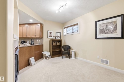 This versatile room features neutral-toned carpet, light-colored walls, and a built-in wet bar with wood cabinetry and a backsplash - 13 841 156 Street, Edmonton, AB - Indoor