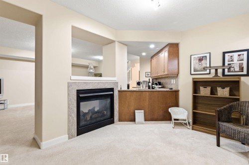 This inviting space features a fireplace with a stone surround, plush carpeting, and a wet bar with wooden cabinetry - 13 841 156 Street, Edmonton, AB - Indoor With Fireplace