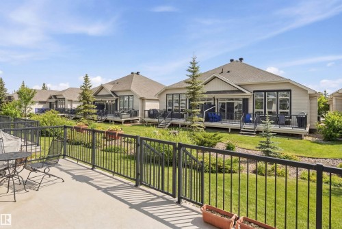 The property features a spacious rear patio with a metal railing, overlooking a landscaped yard with green grass and mature trees - 13 841 156 Street, Edmonton, AB - Outdoor With Deck Patio Veranda With Exterior