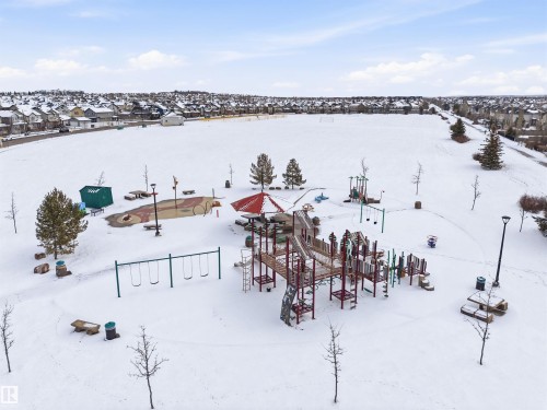 This community park features a large snow-covered playground area with swings, slides, and climbing structures, surrounded by bare trees and benches - 13 841 156 Street, Edmonton, AB - Outdoor With Body Of Water With View