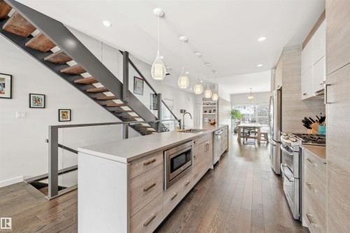 The property features an open-concept living space with hardwood floors, a contemporary staircase with glass railings, and a modern kitchen with light-toned cabinetry and stainless steel appliances - 10607 127 Street, Edmonton, AB - Indoor Photo Showing Kitchen With Upgraded Kitchen