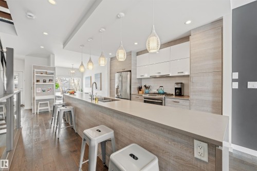 The kitchen features hardwood floors, an extensive island with a sink and pendant lighting, stainless steel appliances, and sleek cabinetry - 10607 127 Street, Edmonton, AB - Indoor Photo Showing Kitchen With Double Sink With Upgraded Kitchen