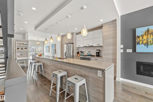 The kitchen features a large island with seating, pendant lighting, stainless steel appliances, and wood flooring - 10607 127 Street, Edmonton, AB - Indoor Photo Showing Kitchen With Upgraded Kitchen