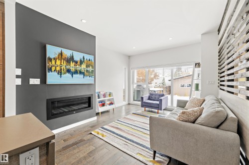 Living area featuring hardwood flooring, a modern fireplace integrated into a dark accent wall, recessed lighting, and large sliding glass doors providing outdoor views - 10607 127 Street, Edmonton, AB - Indoor Photo Showing Living Room With Fireplace