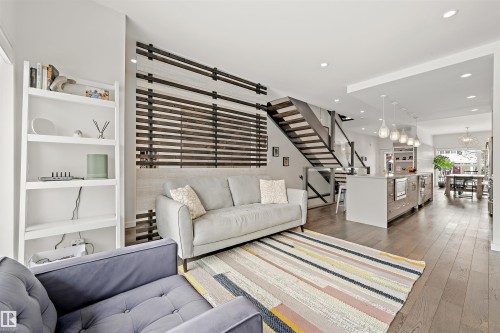 The living area showcases hardwood floors, a modern open staircase with glass and metal railings, and recessed lighting - 10607 127 Street, Edmonton, AB - Indoor Photo Showing Living Room