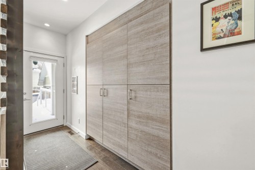 Entryway featuring wood flooring, a built-in storage unit with light wood-look paneling and modern handles, and a glass-paneled door - 10607 127 Street, Edmonton, AB - Indoor Photo Showing Other Room