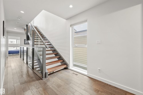 The property features wide plank hardwood flooring, a modern staircase with wood treads and a glass railing, and recessed ceiling lighting - 10607 127 Street, Edmonton, AB - Indoor Photo Showing Other Room