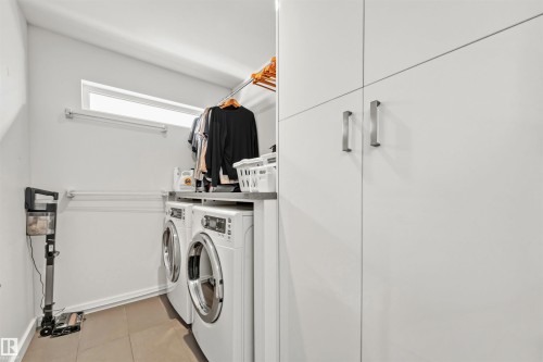 Utility room featuring a window for natural light, white front-loading washing machine and dryer, and built-in white cabinetry with chrome hardware - 10607 127 Street, Edmonton, AB - Indoor Photo Showing Laundry Room
