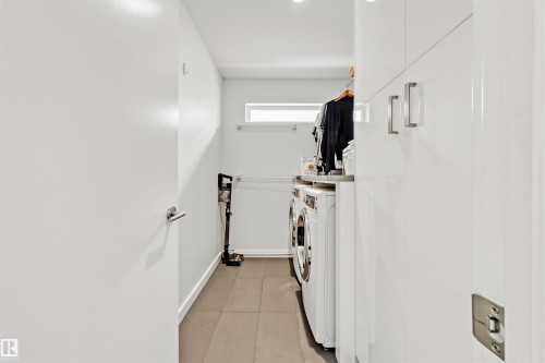 This laundry area features white cabinetry with sleek handles, a front-loading washing machine, and a dryer - 10607 127 Street, Edmonton, AB - Indoor